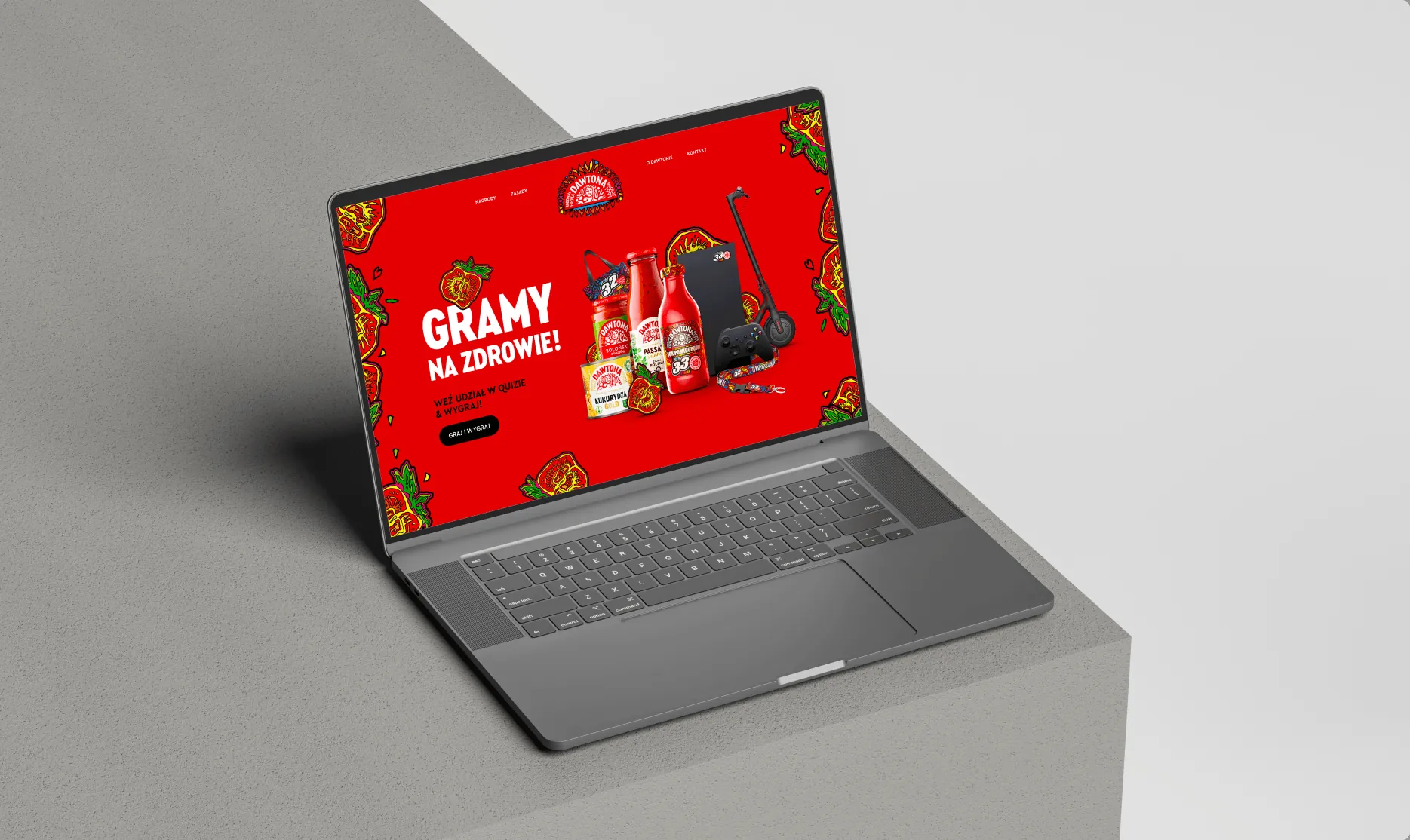 Laptop na szarym postumencie ze stroną mocpomidora.pl: „Gramy na zdrowie!” na czerwonym tle z pomidorami.