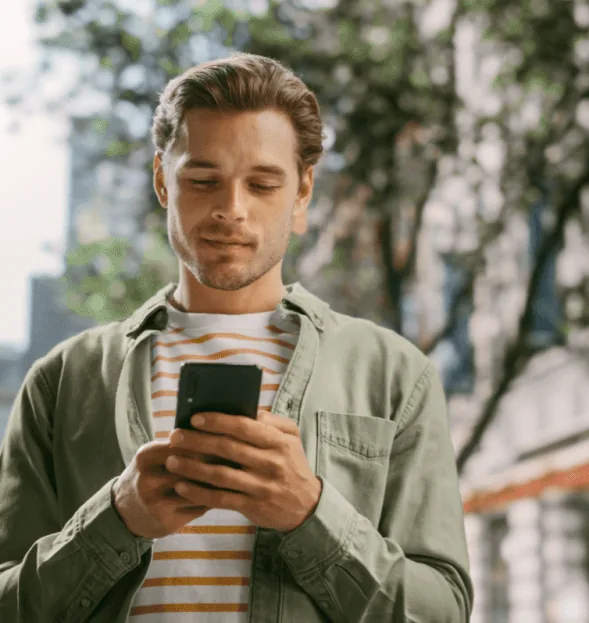 Mężczyzna w oliwkowej koszuli patrzy w telefon na ulicy.
