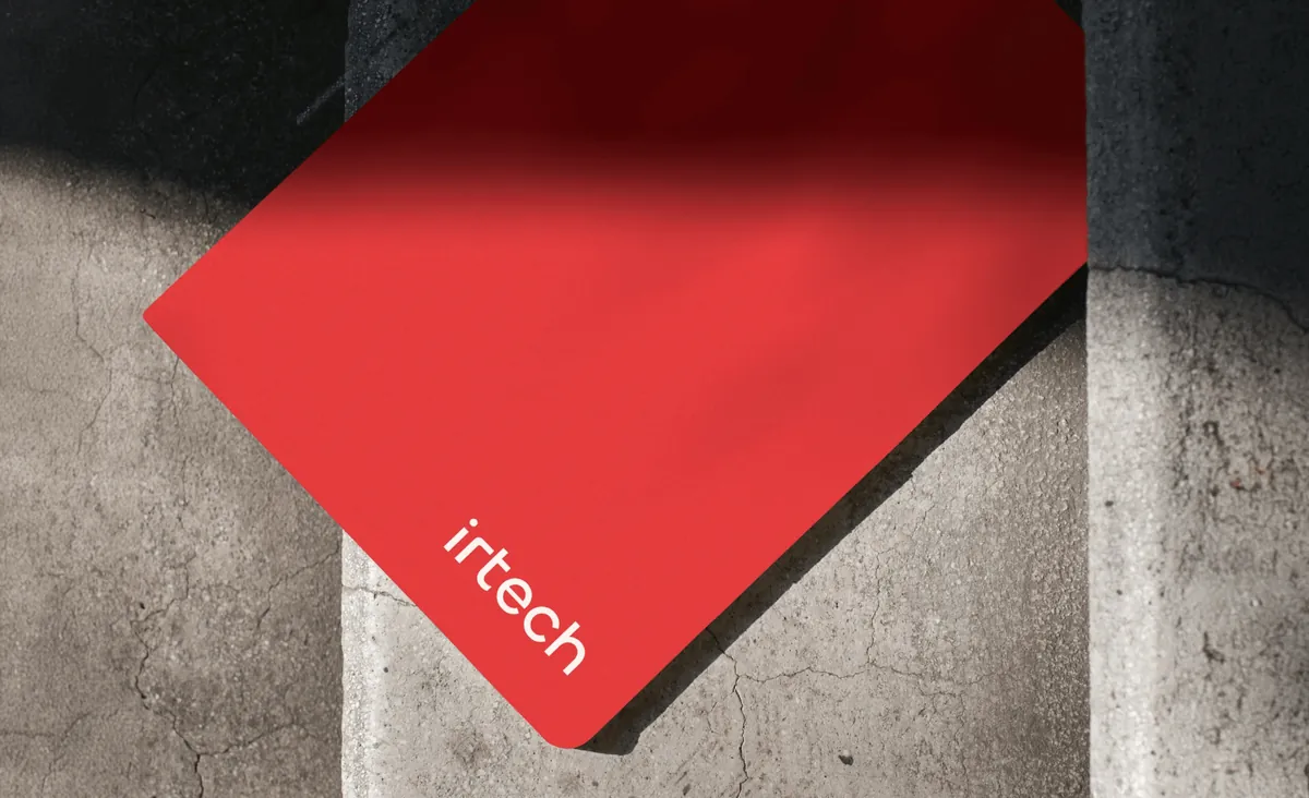 Czerwony notes irtech z białym logo na betonowym murku, w ostrym słońcu.