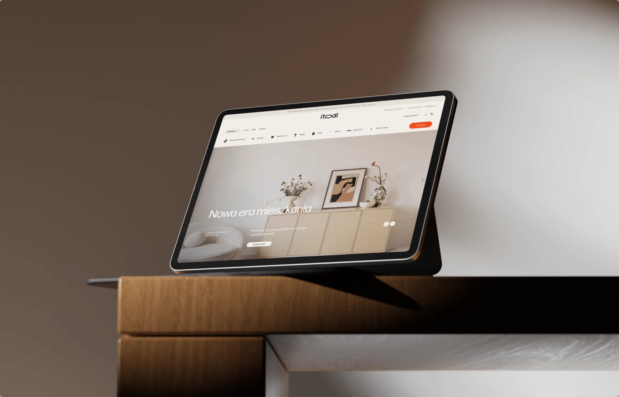 Tablet na drewnianym klocku przy ciemnej ścianie, na ekranie strona główna sklepu itodi ze zdjęciem jasnego salonu.