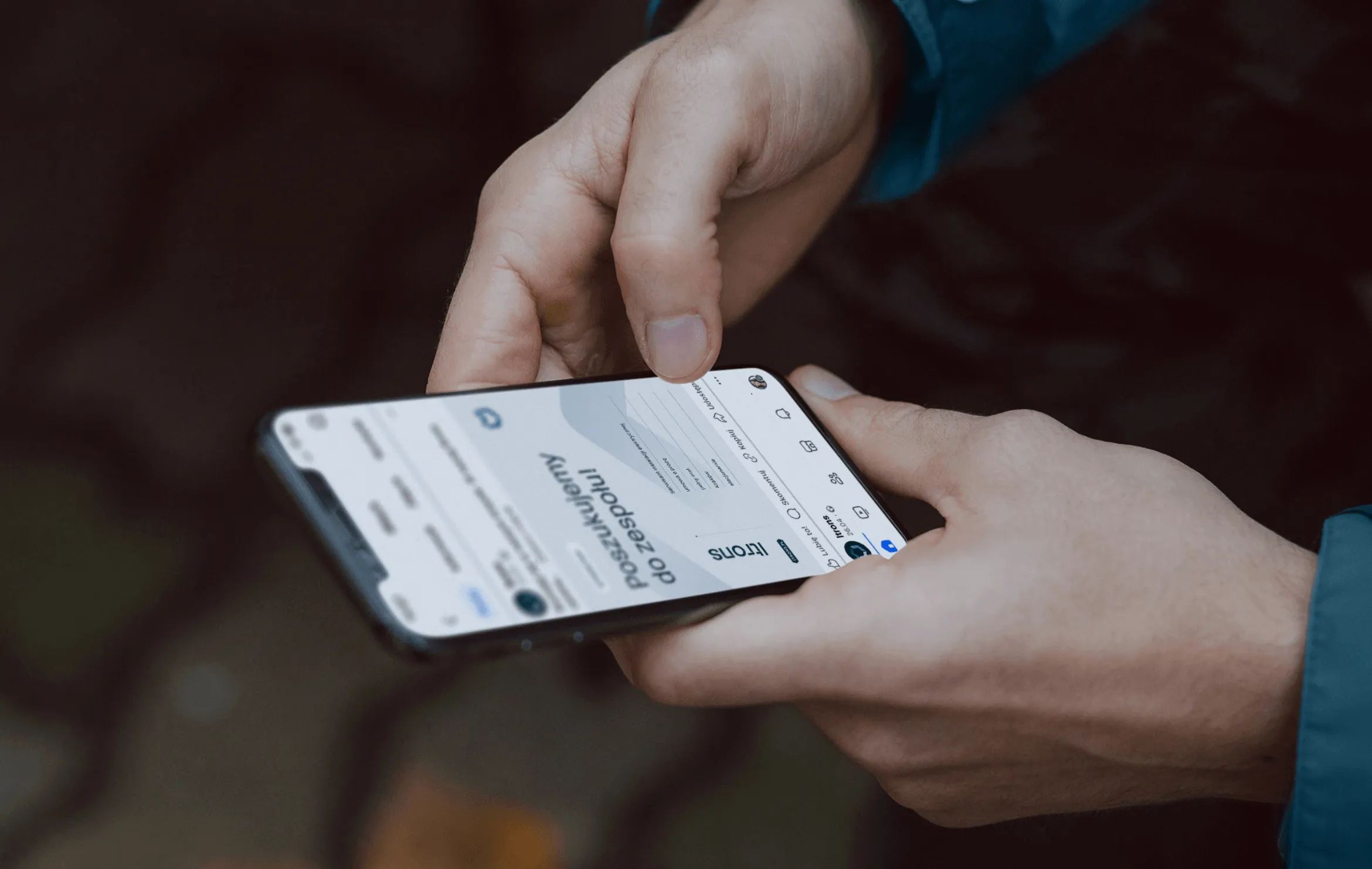 Dłonie trzymające telefon z postem rekrutacyjnym Itrons „Poszukujemy do zespołu”.