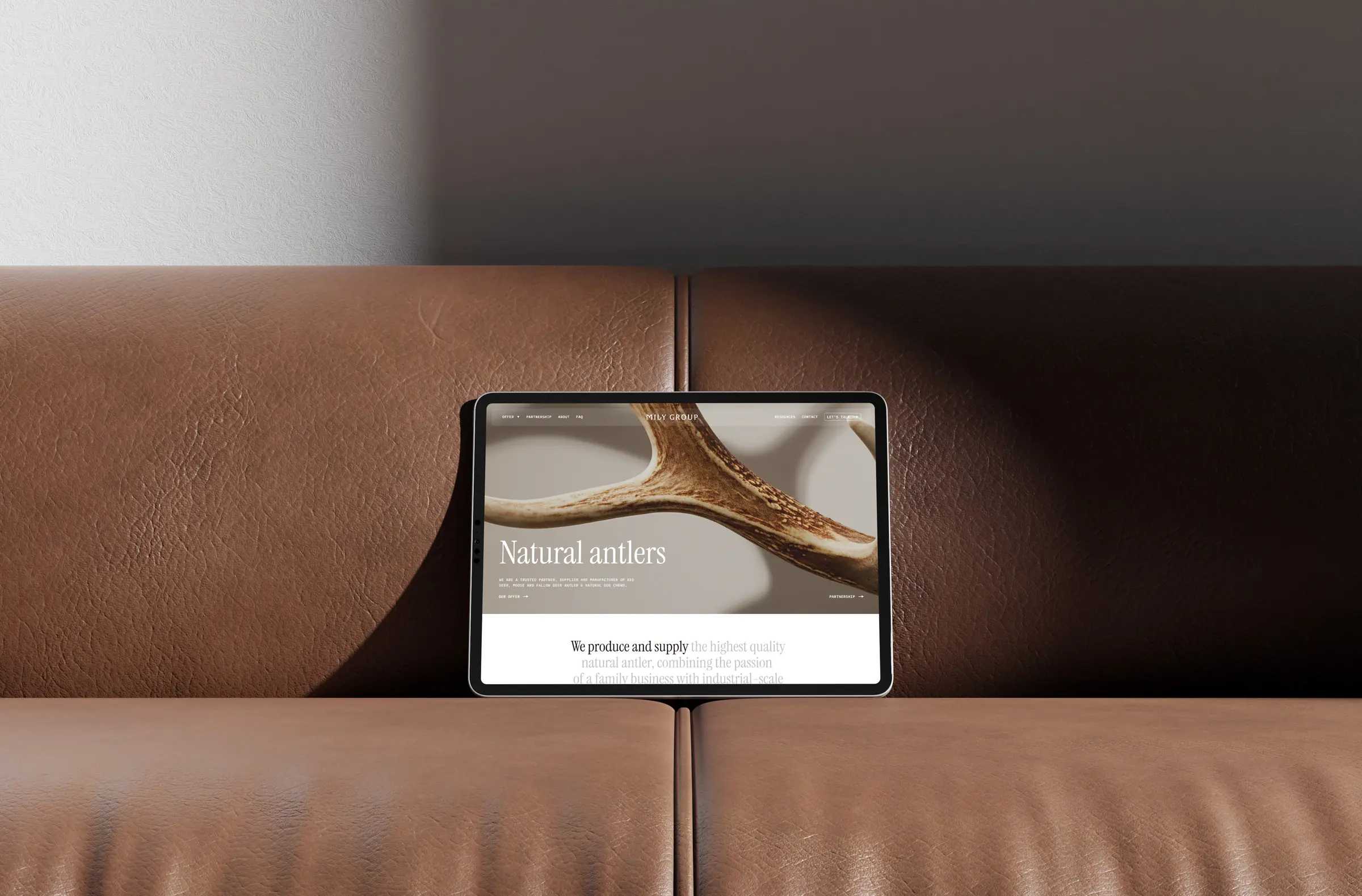 Tablet ze stroną milygroup.com oparty o brązową skórzaną kanapę.