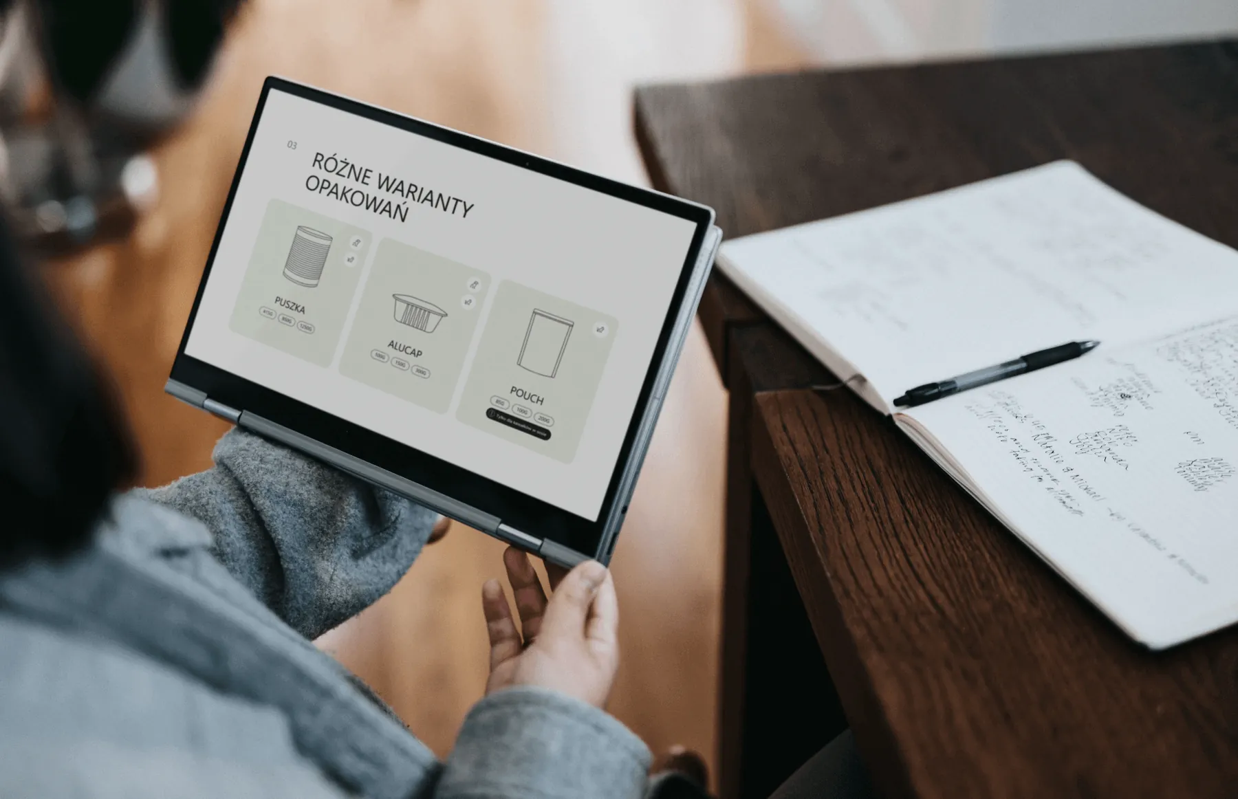 Tablet z podstroną wariantów opakowań PetCuisine, obok notatnik