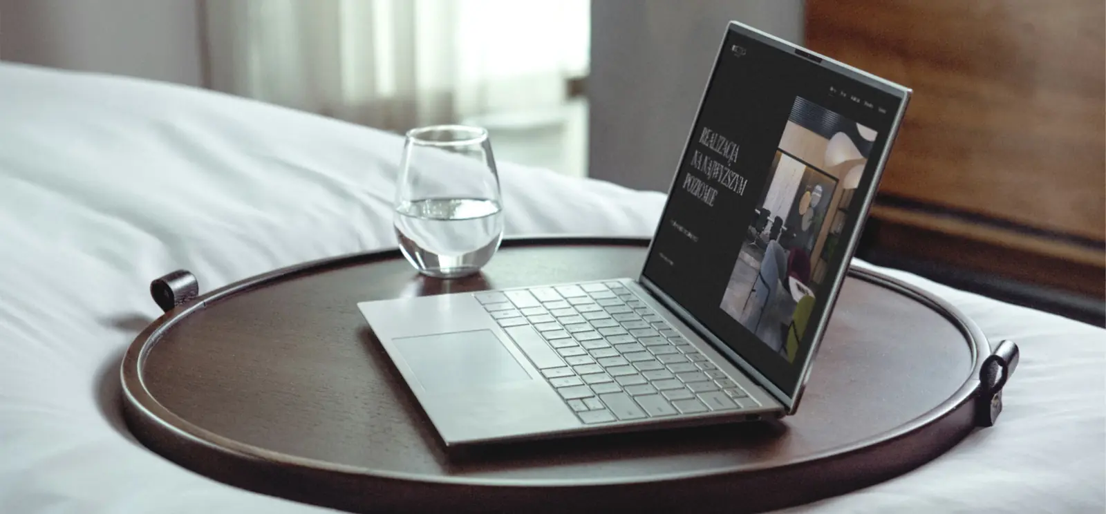 Laptop ze stroną Septima Design na tacy przy hotelowym łóżku.