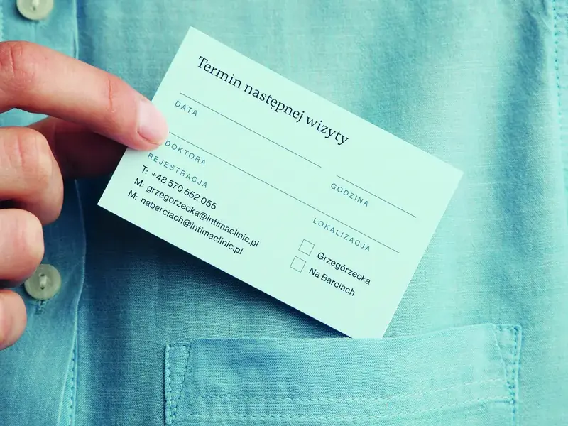 Miętowa karta Intima Clinic z terminem kolejnej wizyty wsuwana do kieszeni koszuli.