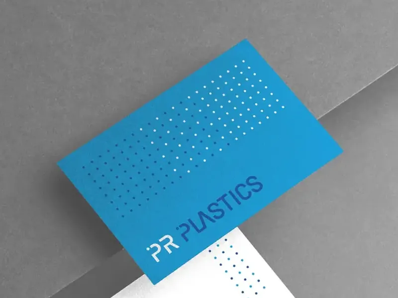 Niebieska wizytówka PR Plastics z patternem z kropek na szarym papierze.