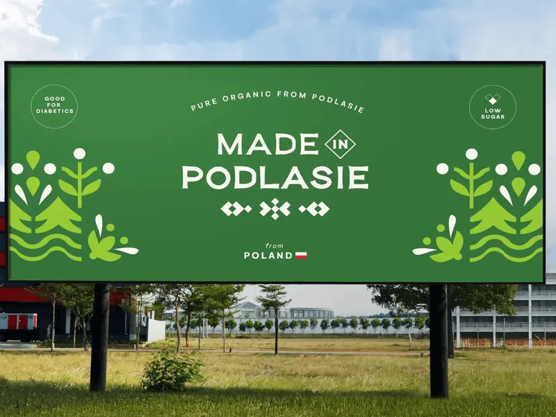 Billboard Made in Podlasie przy drodze: logo, ornament i ilustracje roślin na zielonym tle.